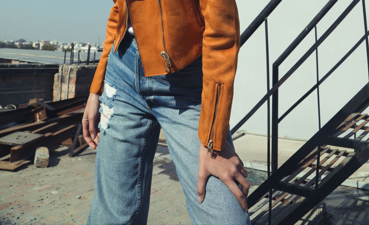 Close-up of a stylish outfit featuring a leather jacket and ripped jeans outdoors.